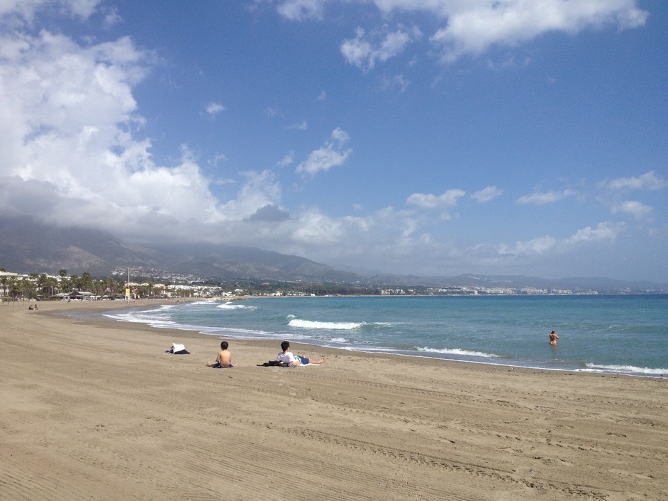 Des gens qui se détendent sur une plage de sable avec des montagnes en arrière-plan.