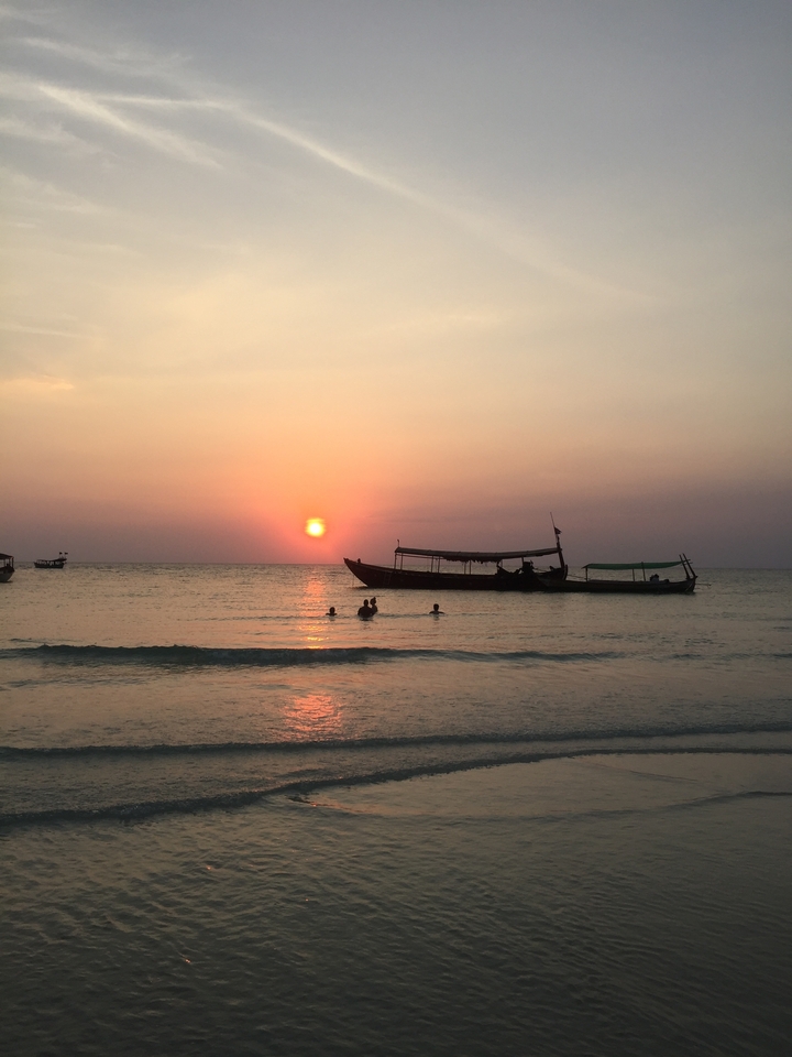 Sunset over the ocean with people swimming.