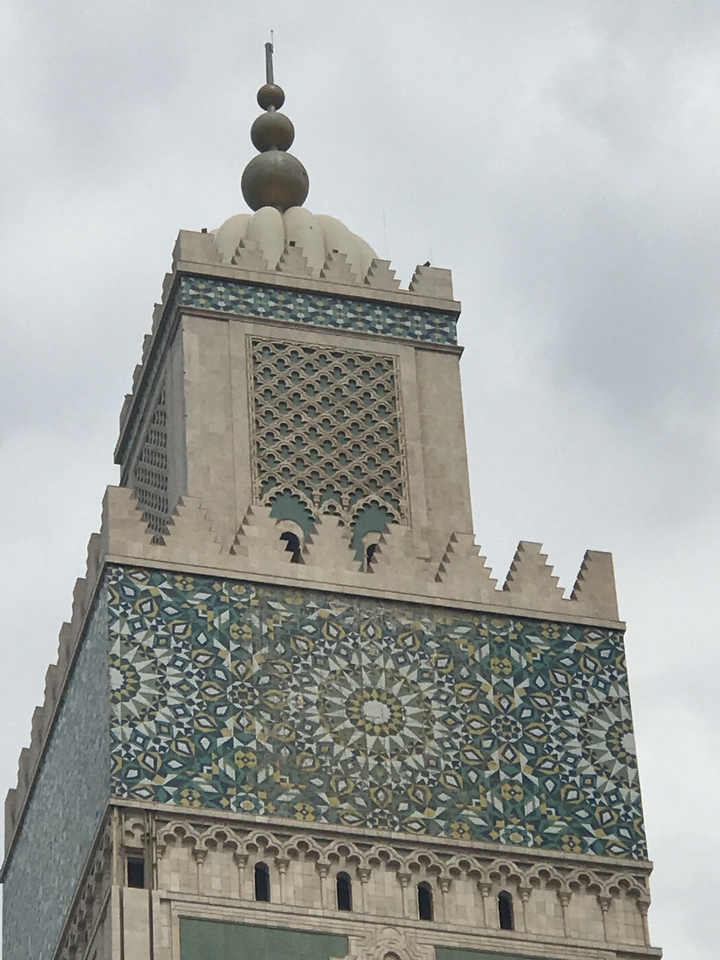 Ornate mosaic minaret against cloudy sky.