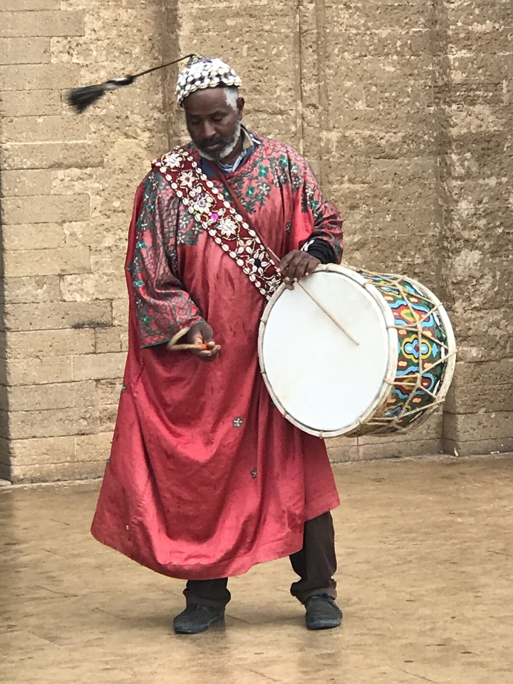 Man in traditional attire playing a large drum.