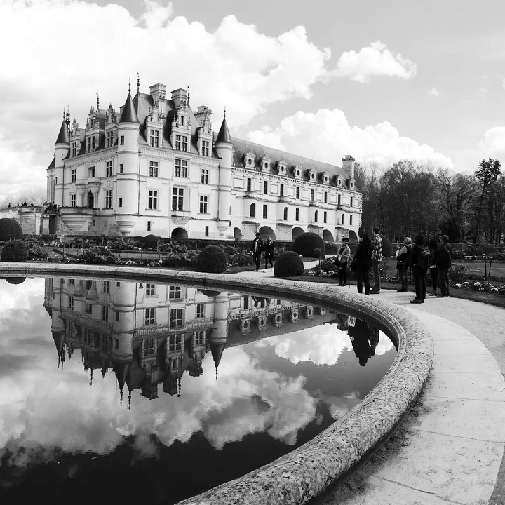 Reflet d'un château dans un étang avec des touristes autour.