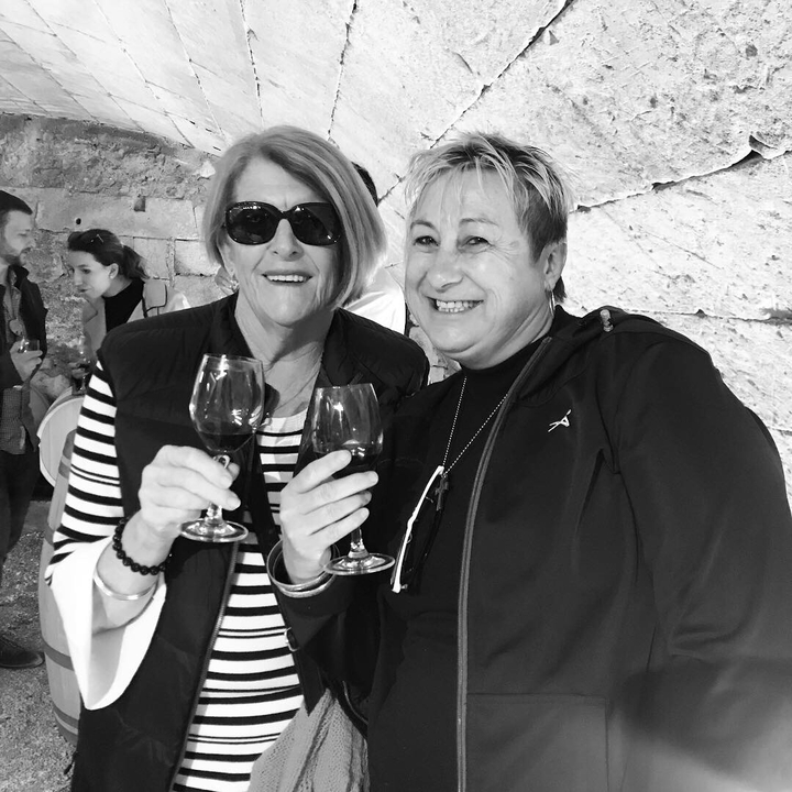 Deux personnes savourant un verre de vin, fond de mur en pierre.