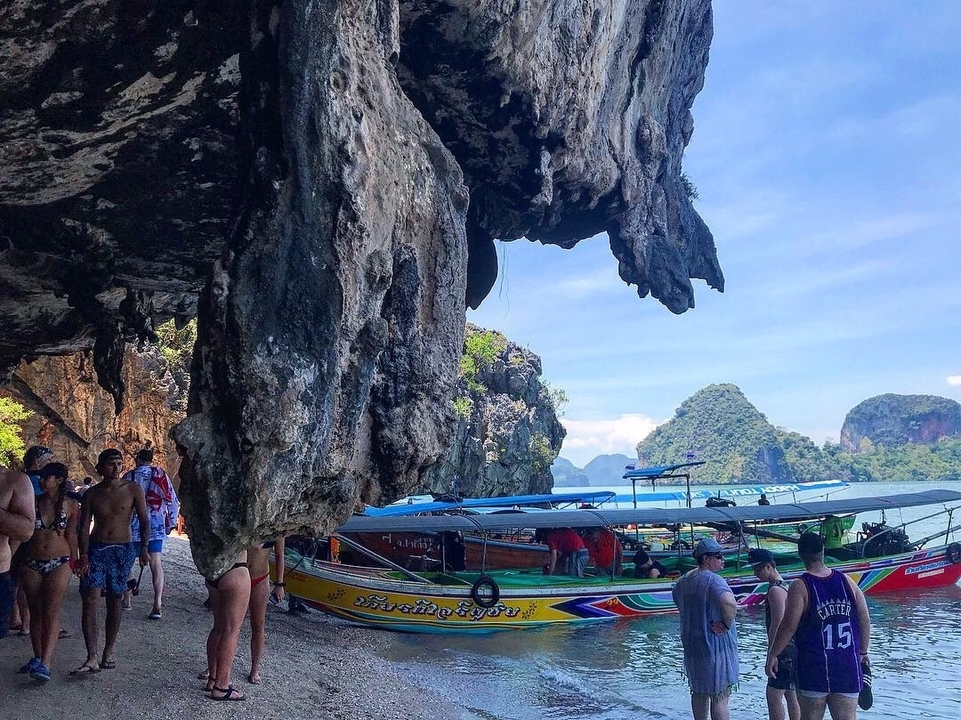 People exploring a rocky area with boats and lush, scenic background.