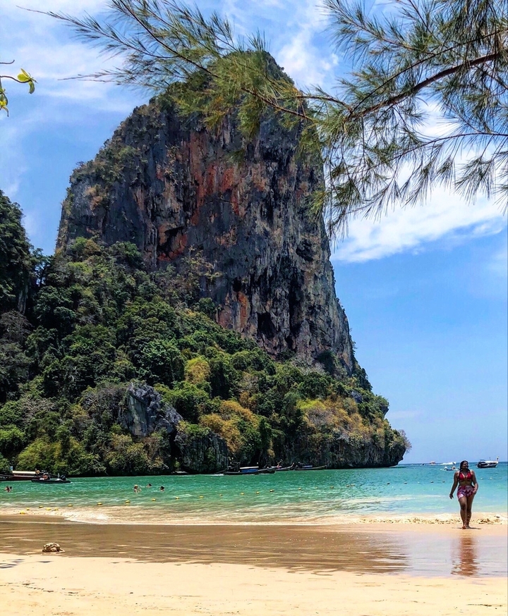 Tall limestone cliff covered with vegetation with a blue sky.