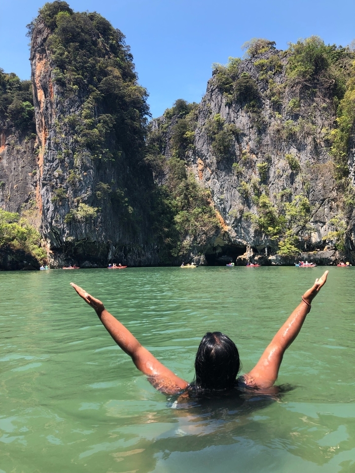 Arms raised from water with limestone cliff background, people kayaking.