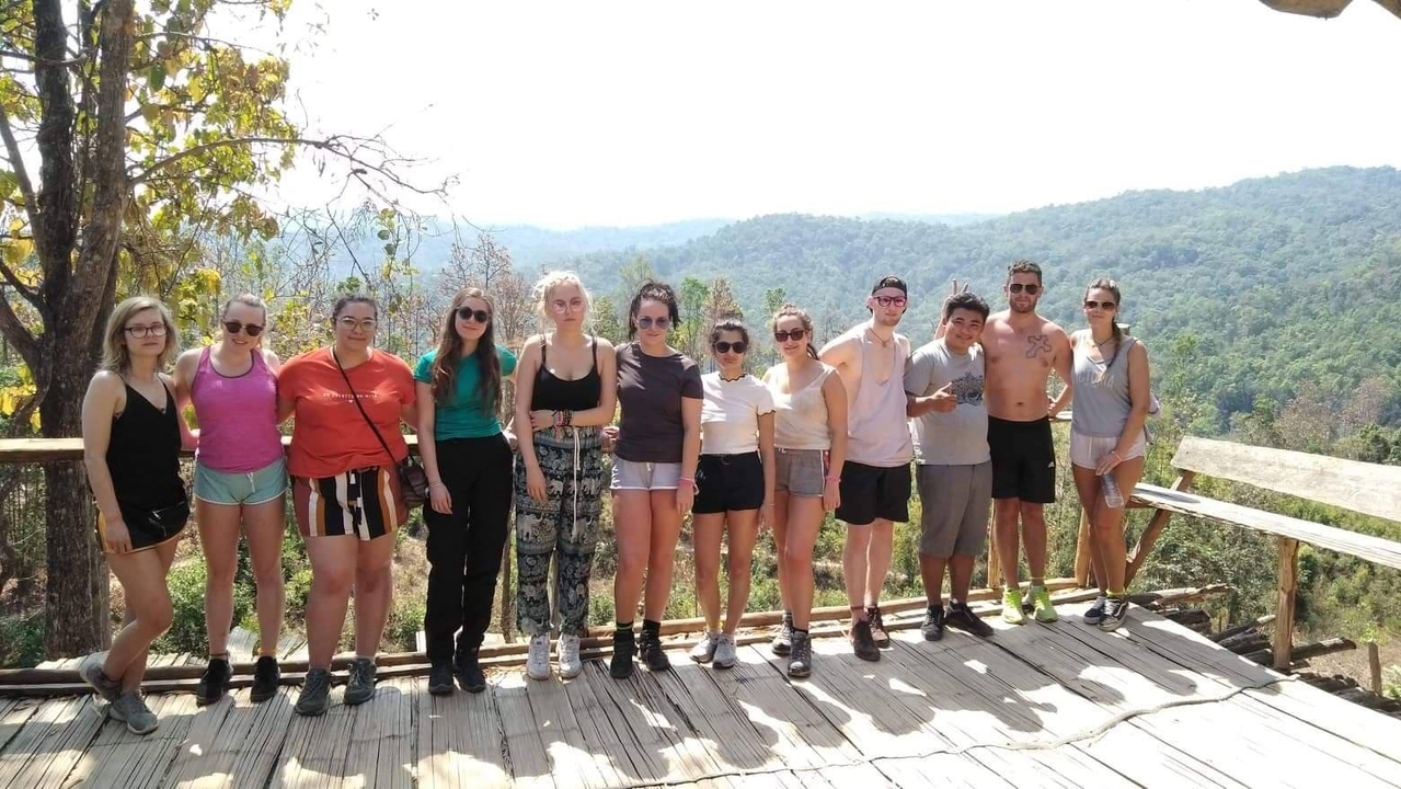 Group of people posing on a deck with forest hills in the background.