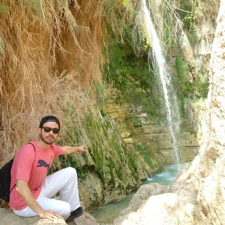 Person pointing towards a waterfall in a rocky area