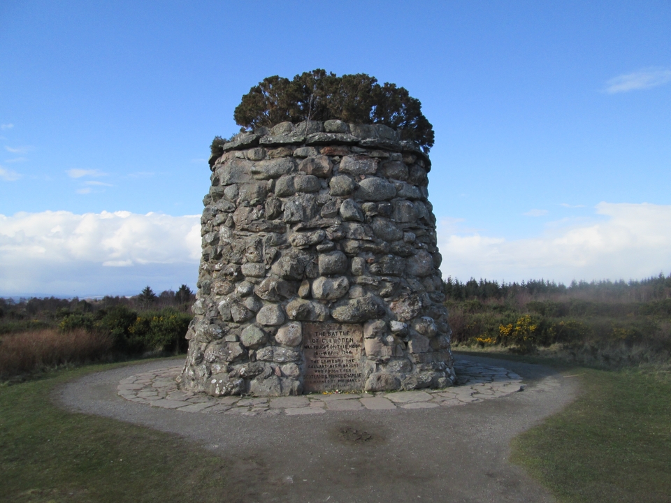 Cairn on a grassy field with a clear sky.