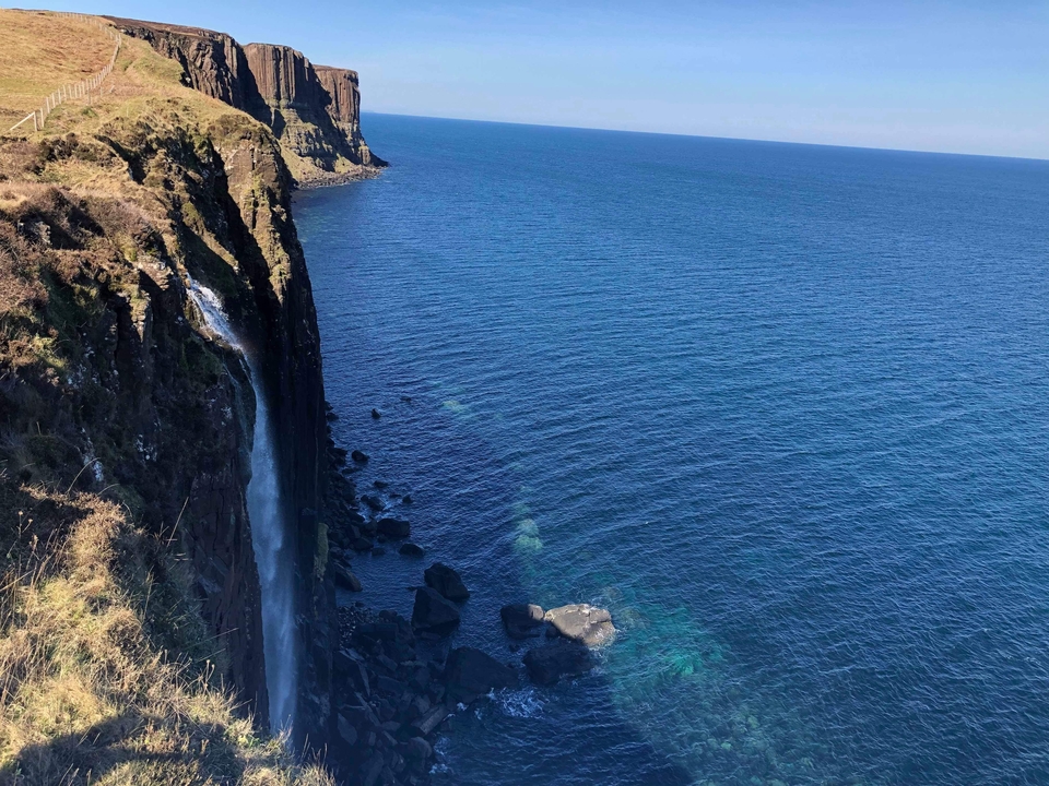 Cliffside waterfall with a clear blue sea.