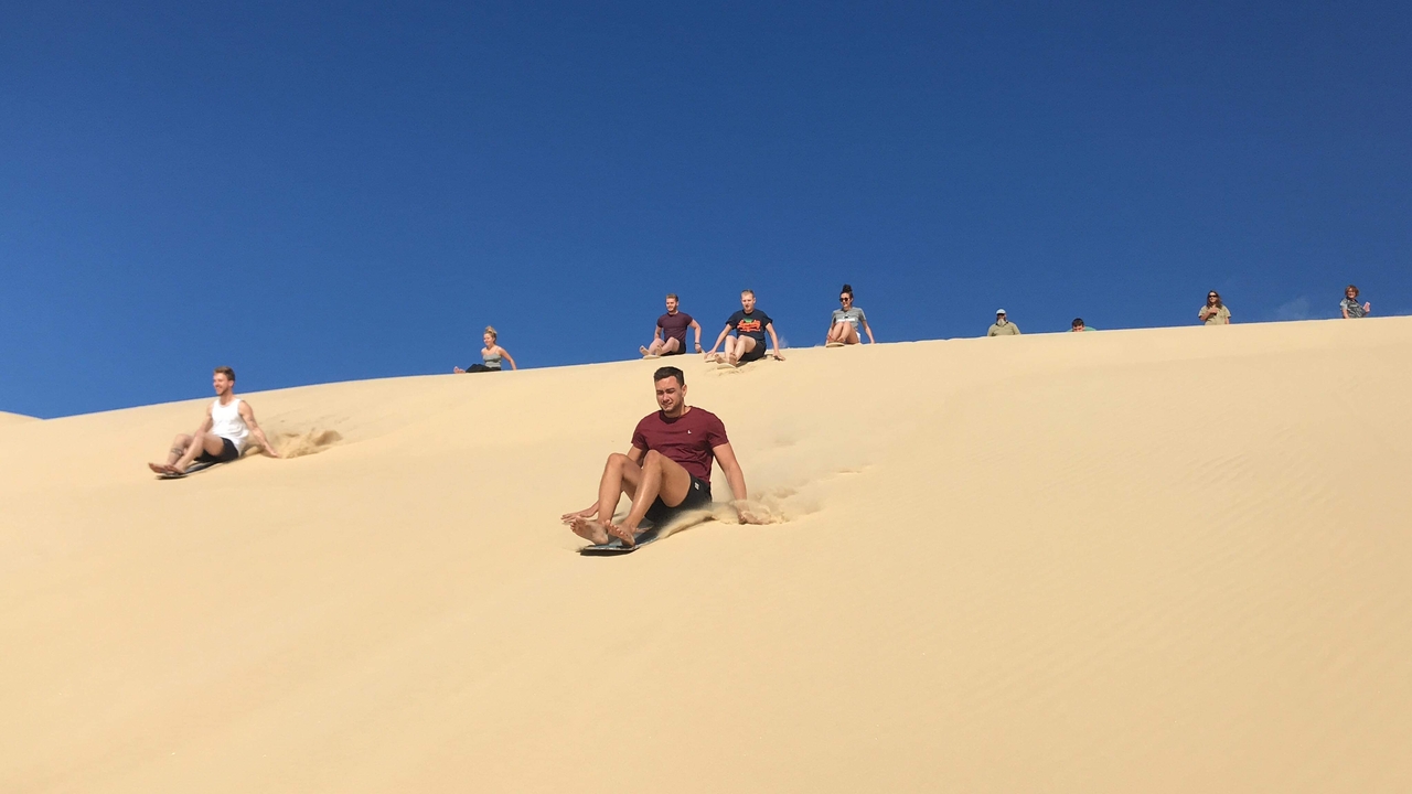 People sliding down sandy dunes enjoying outdoor fun.