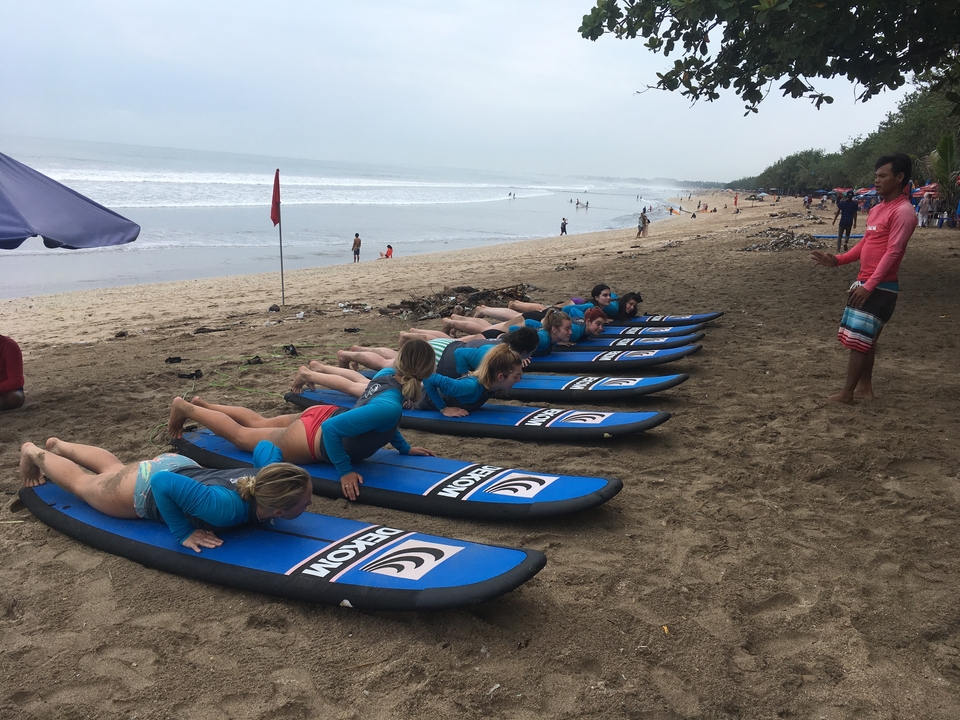 Group learning to surf lying on the sand with surfboards.