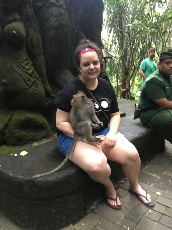 Person sitting with a monkey in a forested area.