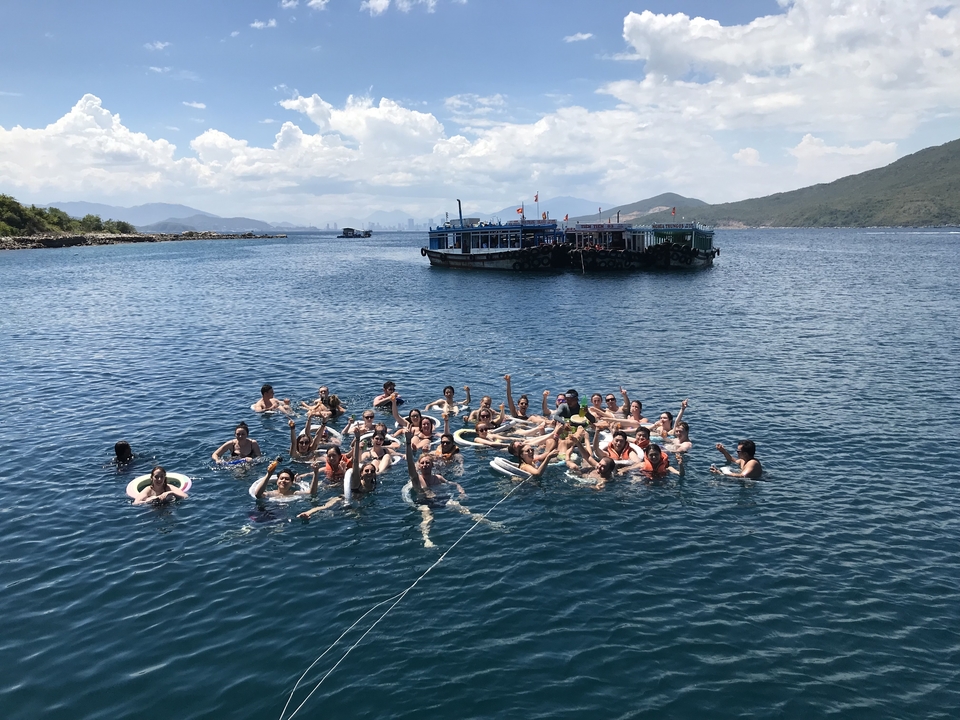Large group swimming in the ocean around a boat with a cloudy sky.