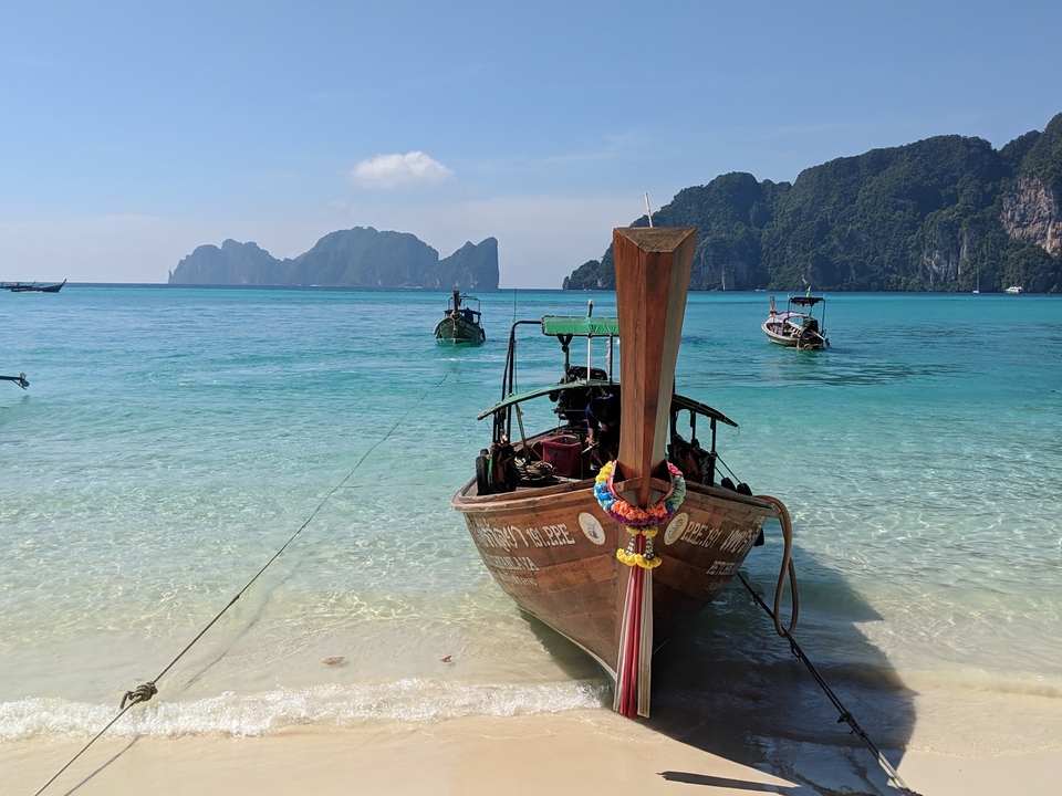 Traditional longtail boat anchored on a clear blue sea with distant islands.