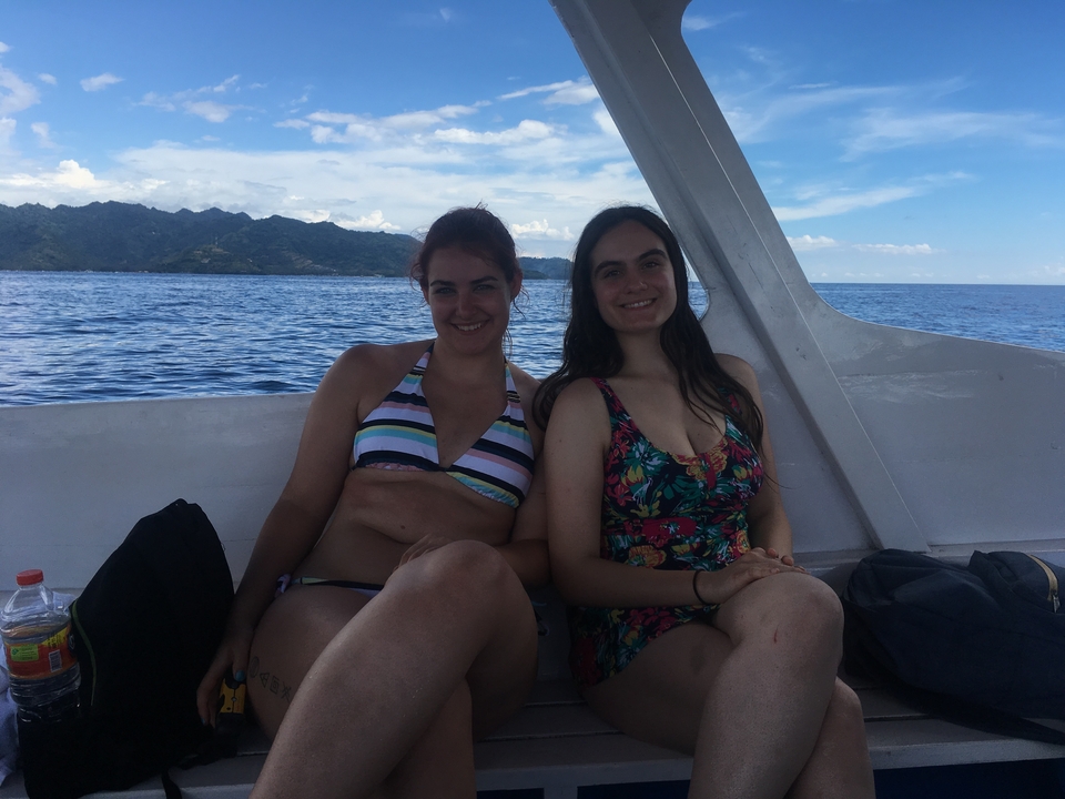 Two women in swimsuits sitting on a boat with mountains in the distance.