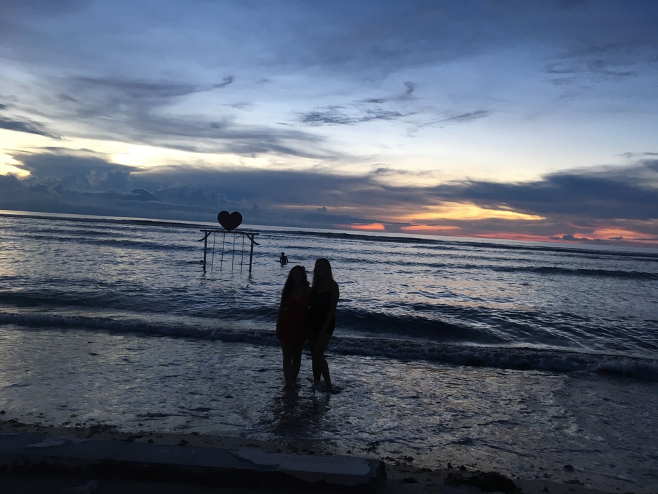 Silhouette of two people standing on the beach during sunset.