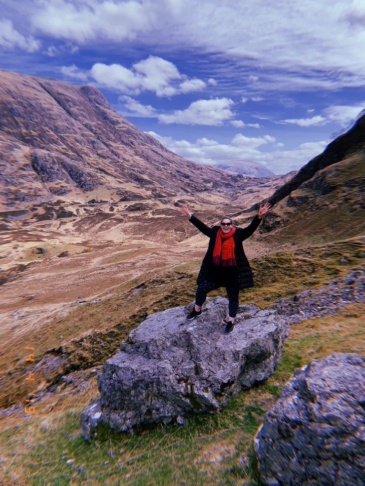 Person posing with arms raised on a rocky landscape.