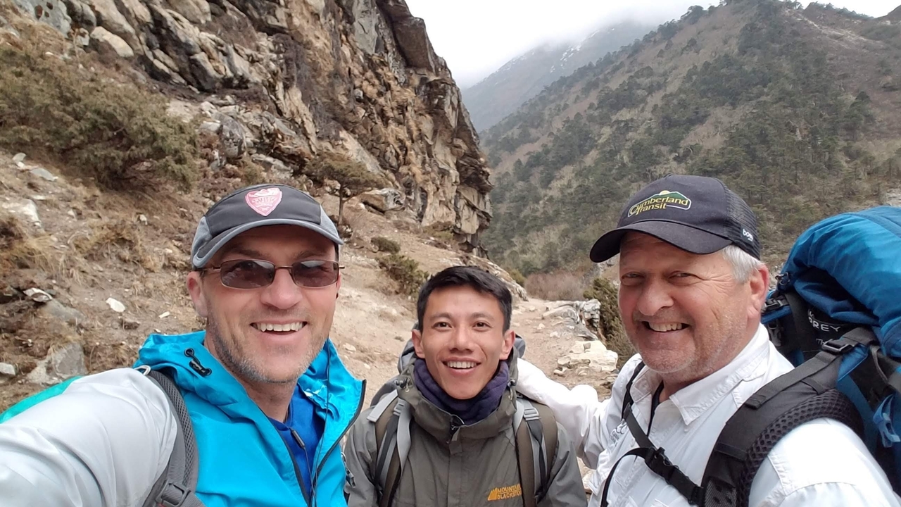 Trois randonneurs posant sur un sentier avec des montagnes.