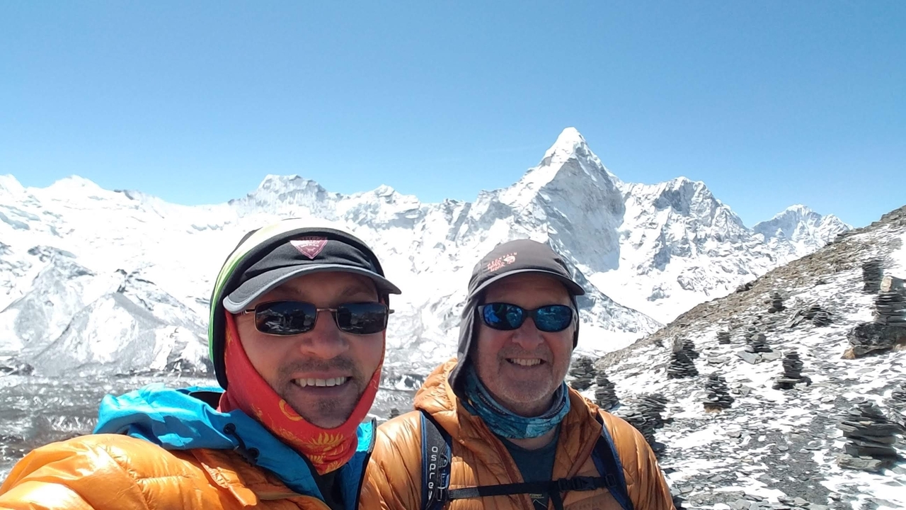 Deux hommes souriants devant des montagnes enneigées.