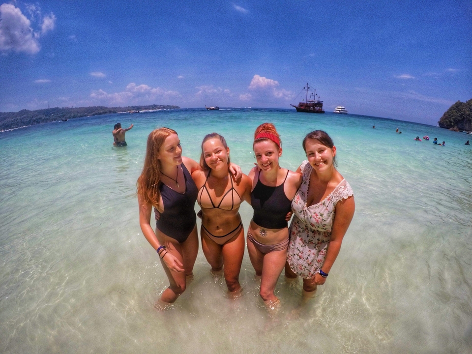 Four women posing at the beach with clear water.