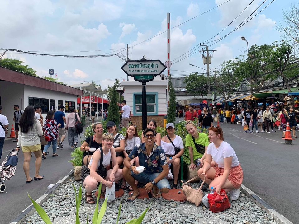 Group of people posing under a sign in a busy outdoor market.