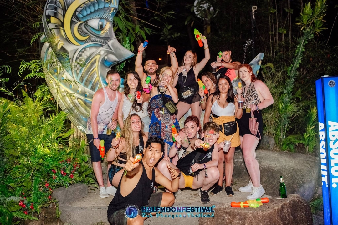 Group of people celebrating with water guns in a garden at night.