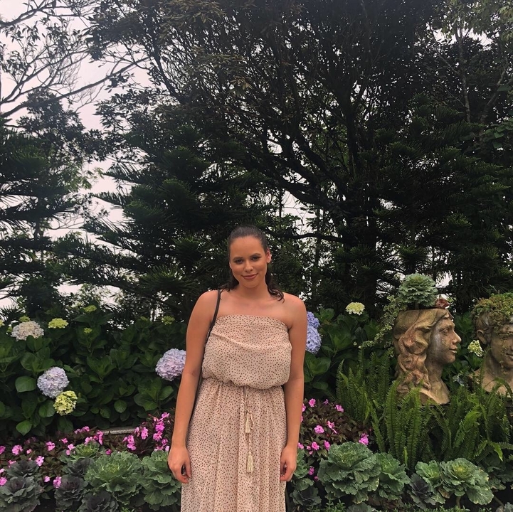 Person standing in a garden with flowers and sculptures.
