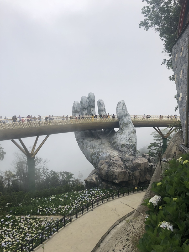 A large hand-shaped structure holding a pedestrian bridge in the fog.