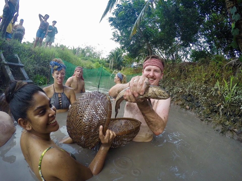 Group of people in a muddy river, one holding a fish.
