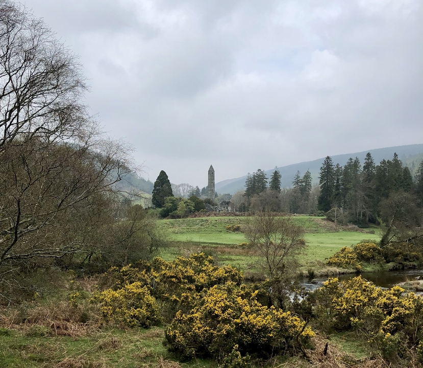 Scenic landscape with ancient tower surrounded by greenery and mountains.