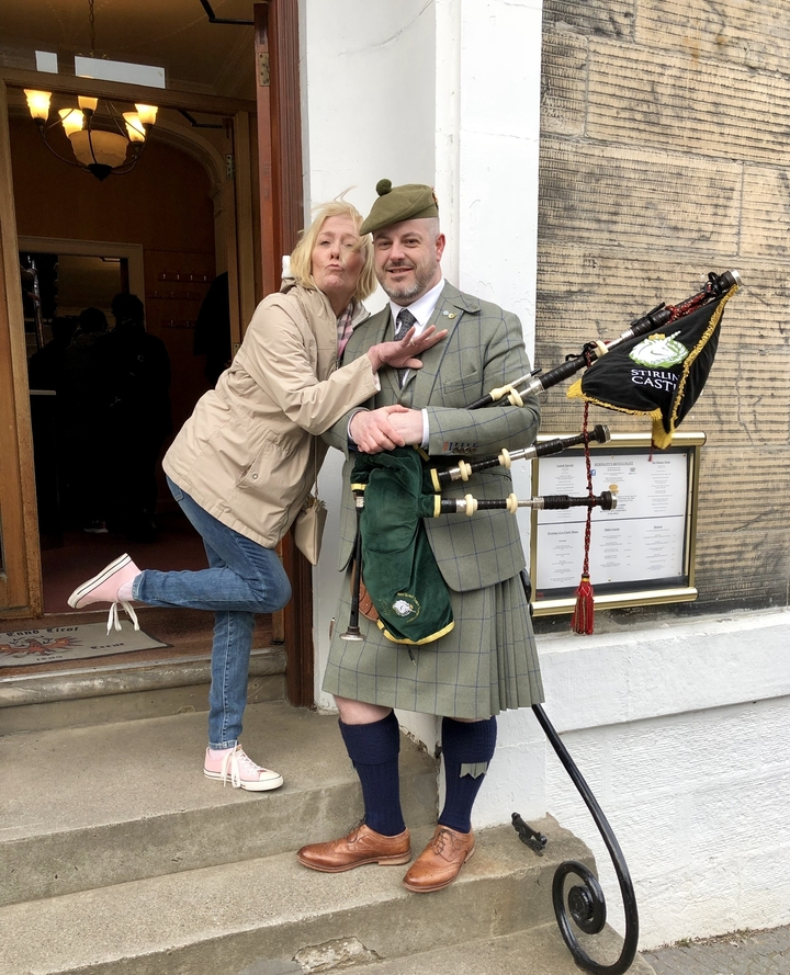 Woman posing with a bagpiper in front of a building.