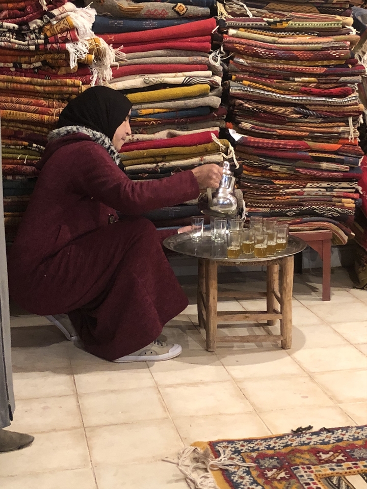 Person pouring tea from a teapot onto a tray of glasses.