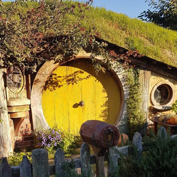 Round yellow door set into a grassy hill, resembling Hobbiton.