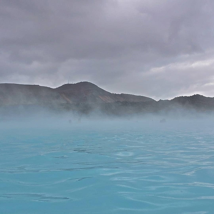 Mist rising over blue thermal waters with hills in the background.