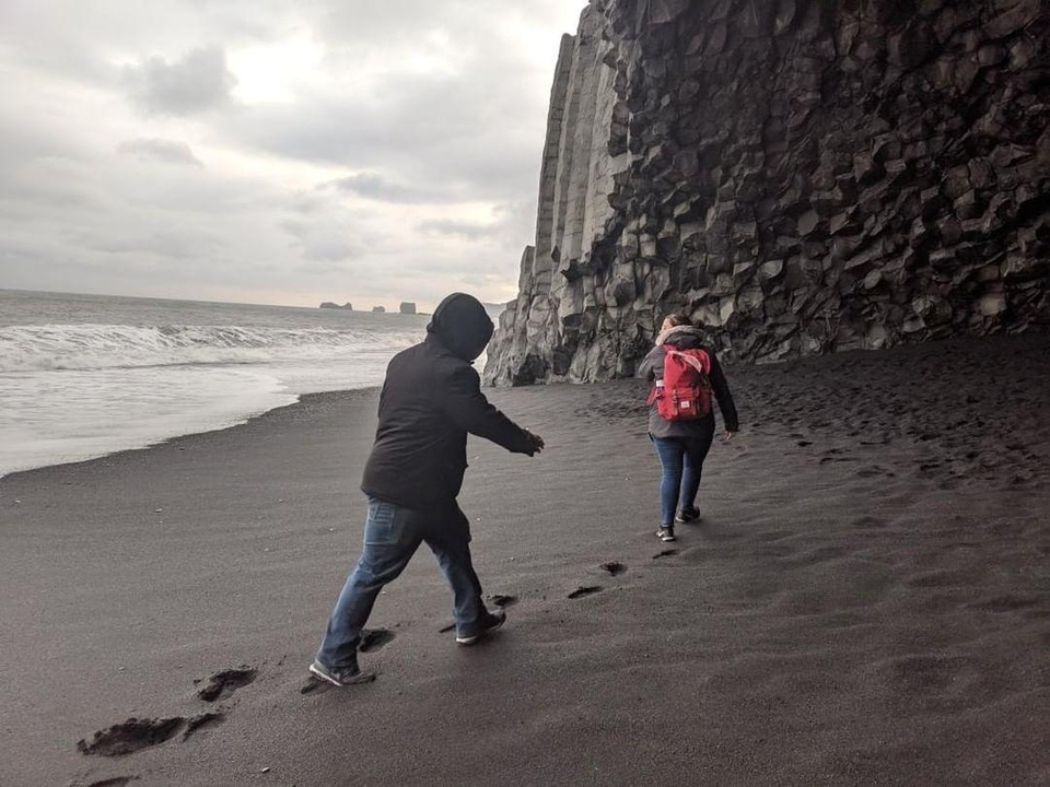 People walking on a sandy beach with rocky cliffs.