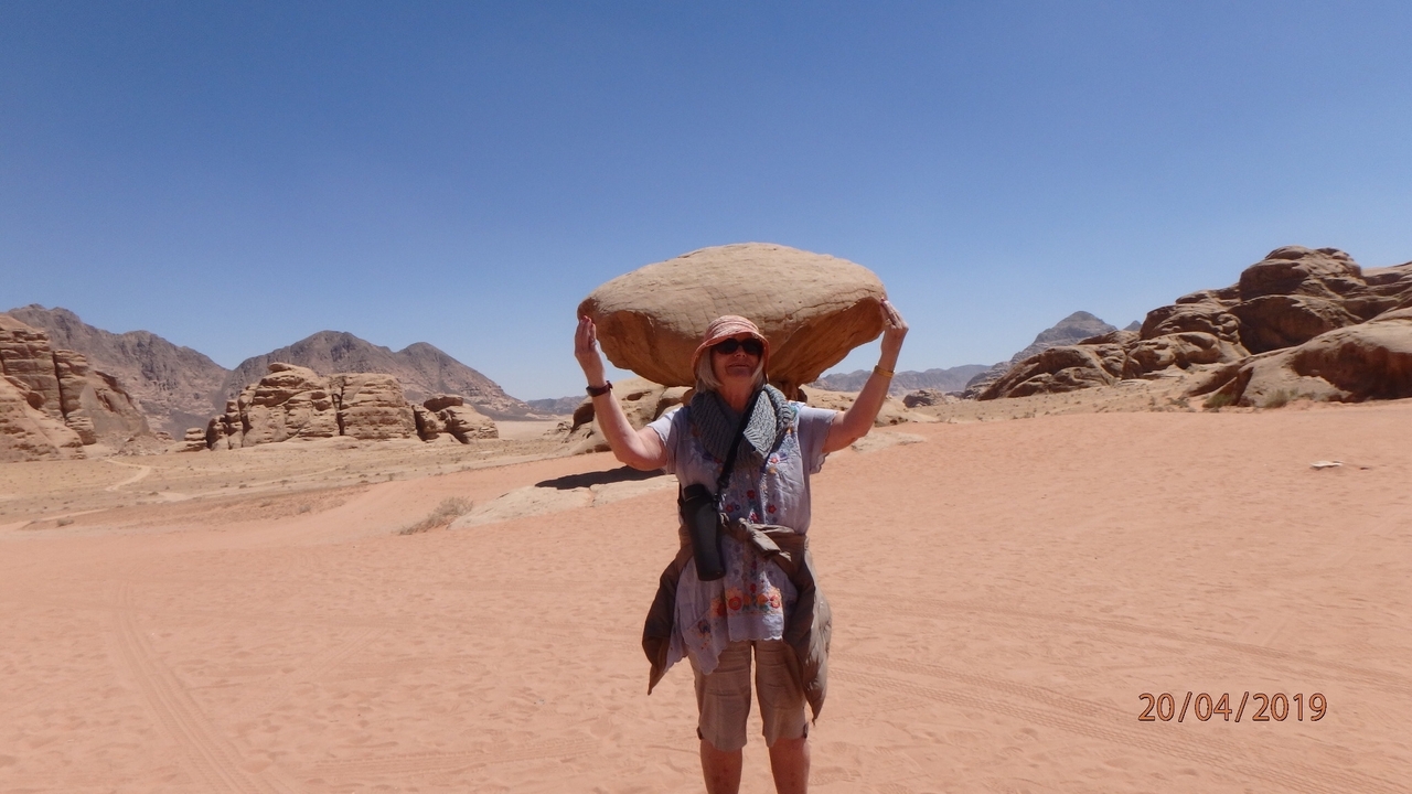 Personne faisant semblant de tenir une grosse pierre au-dessus de sa tête dans un désert.