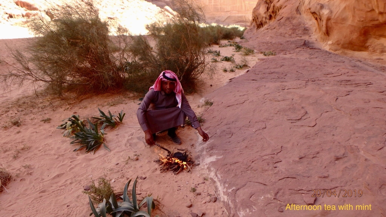 Personne préparant du thé sur un petit feu dans un décor désertique.