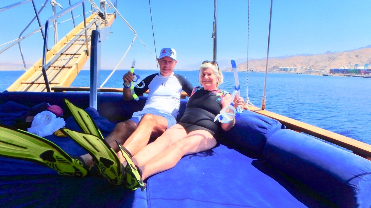 Deux personnes souriantes tenant du matériel de plongée en apnée sur un bateau.