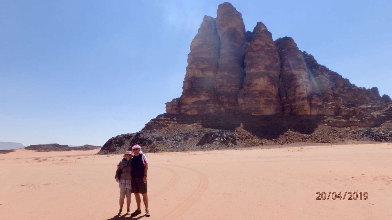 Deux personnes posant devant une grande formation rocheuse dans un désert.