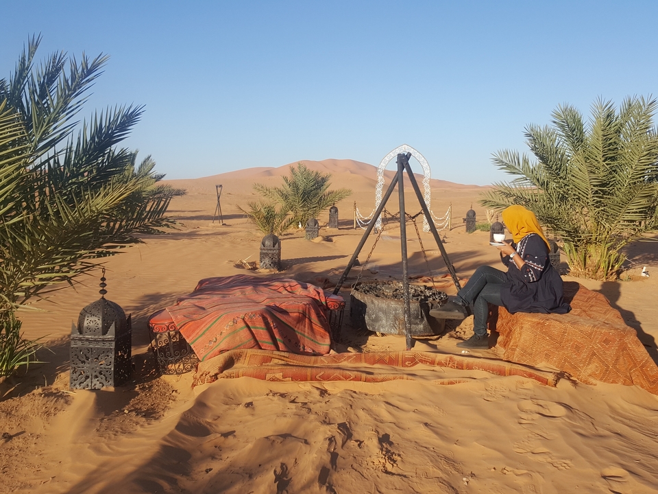 Person enjoying tea in a desert setting with sand dunes.