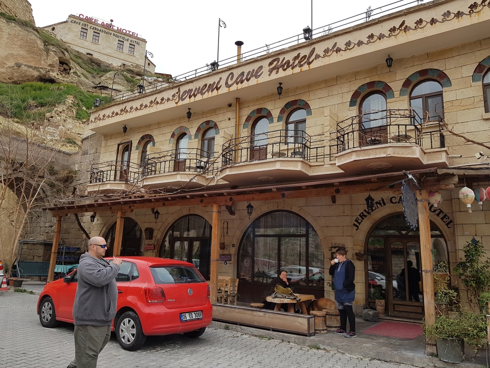 Extérieur d'un hôtel troglodyte avec des personnes et une voiture garée.
