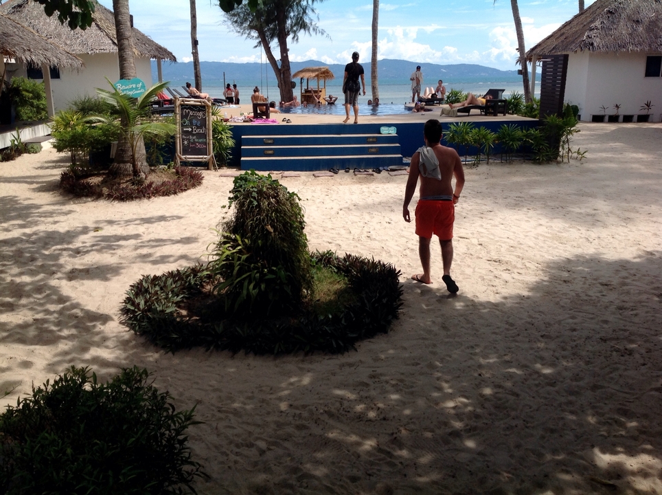 A man walking towards a poolside area with others relaxing on lounge chairs by the water.