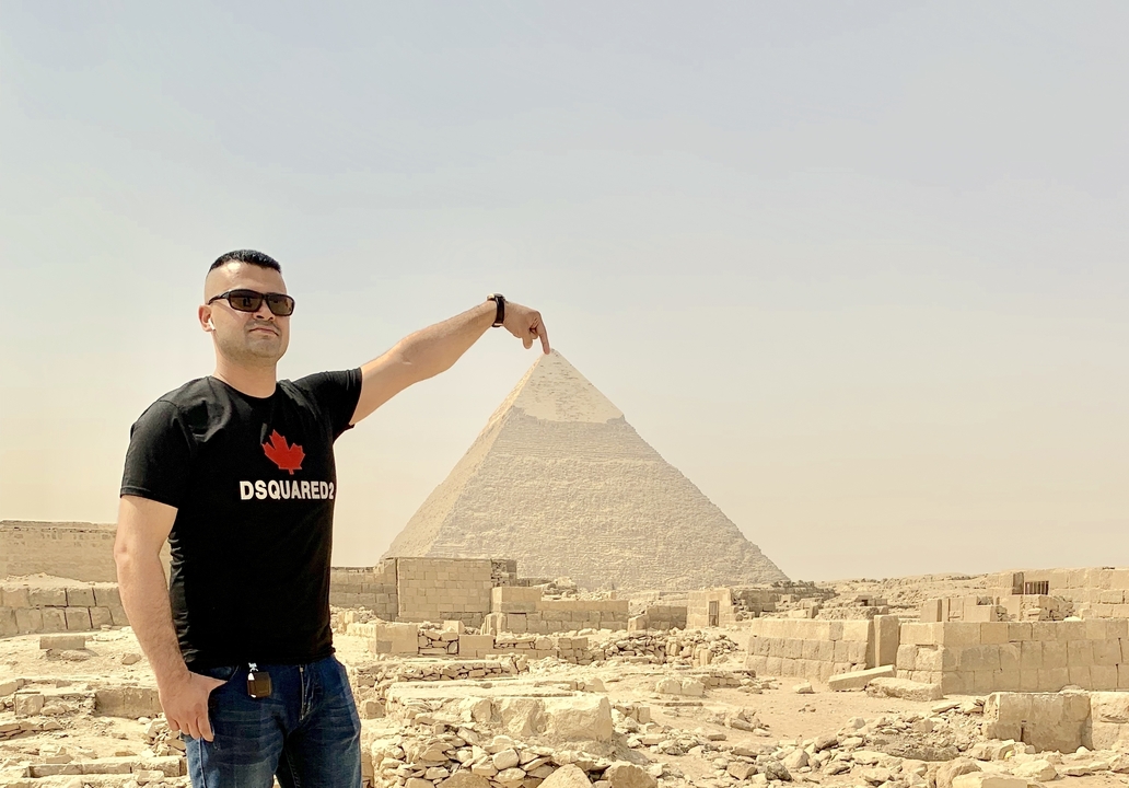 Un homme qui pose de manière ludique avec la Grande Pyramide de Gizeh en arrière-plan.