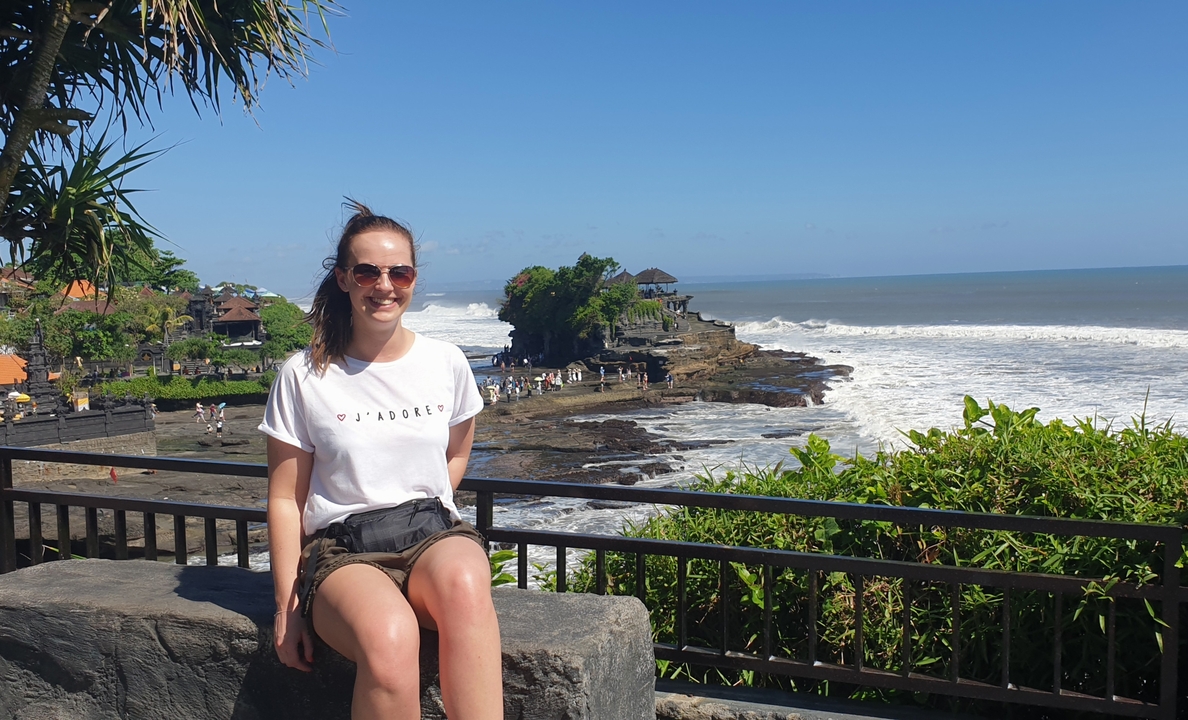 Person sitting by a railing with a view of Tanah Lot.