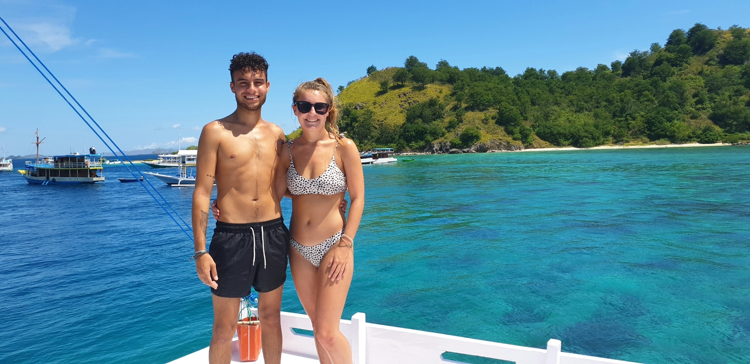 Couple standing on a boat with turquoise waters and lush islands.