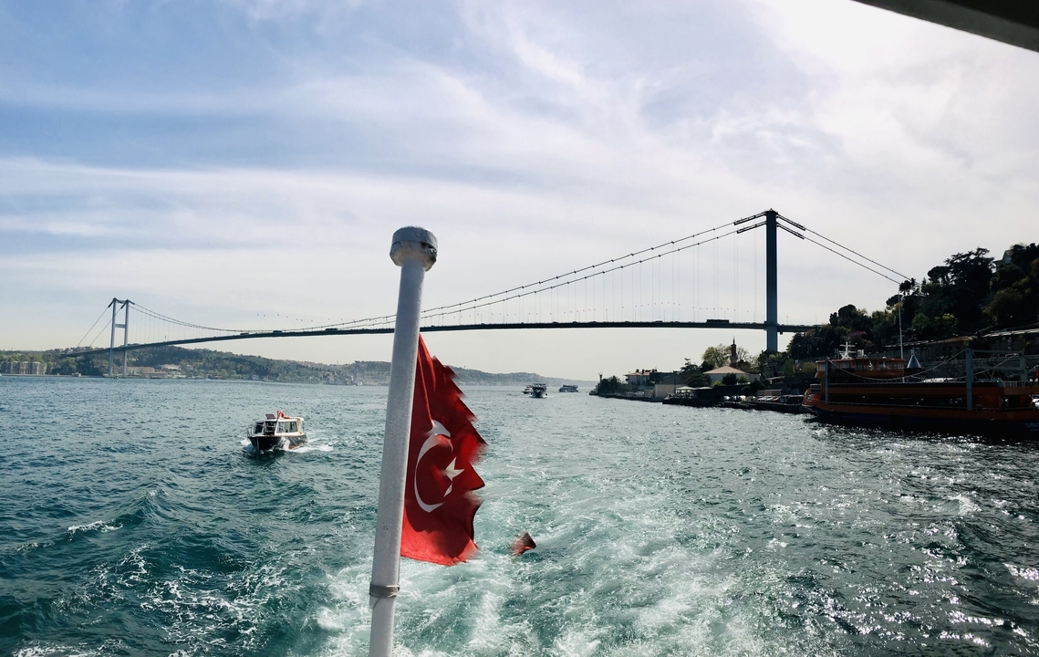 A boat on a sea with a bridge and a Turkish flag.