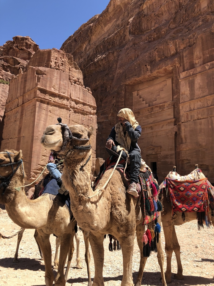 Man riding a camel in front of ancient stone structures