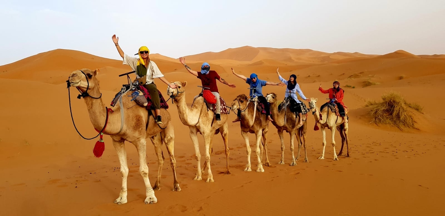 People riding camels in a line through the desert.