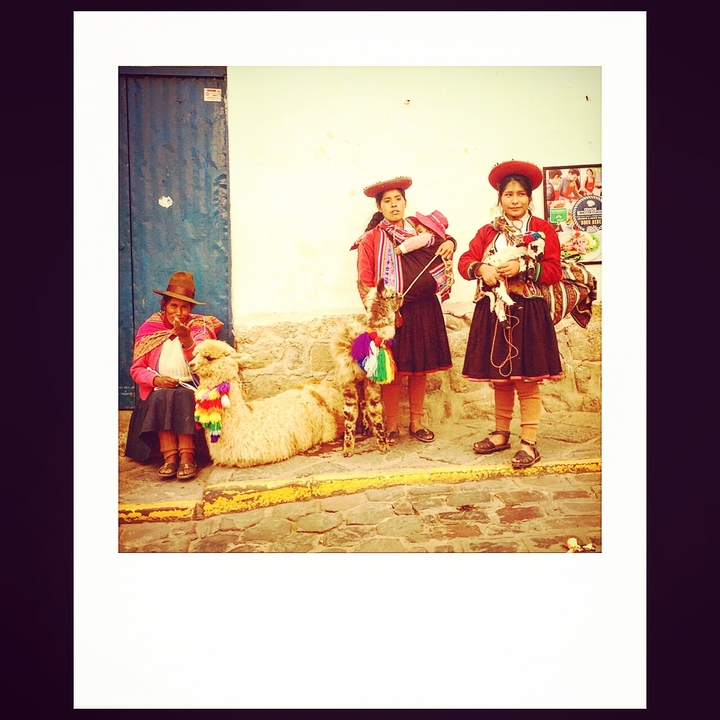 Traditional Peruvian women with llamas on a cobbled street.