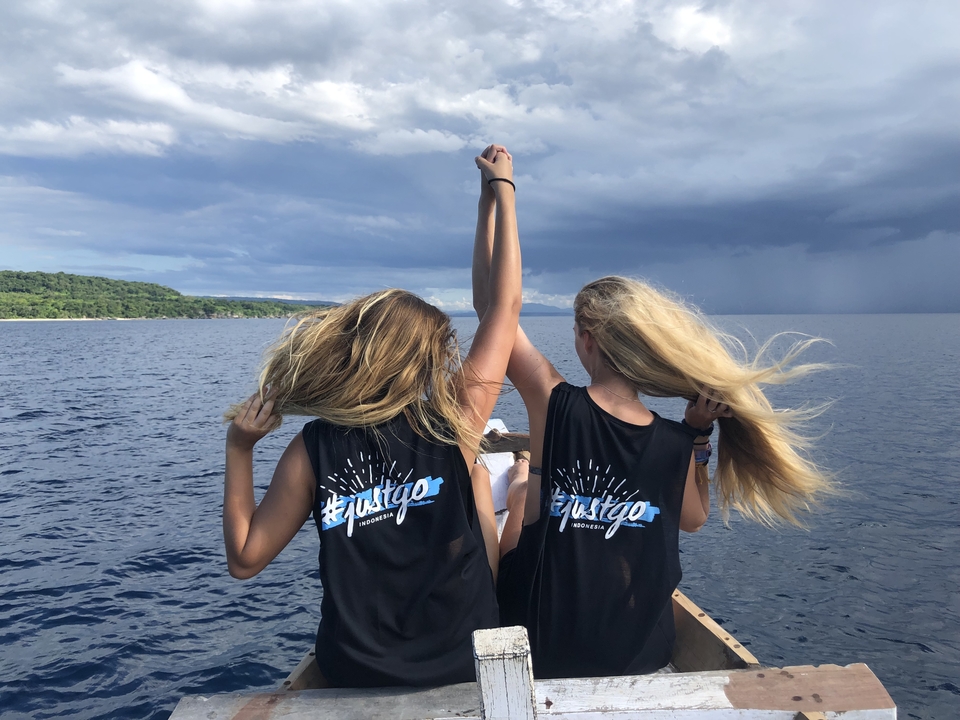 Deux personnes sur un bateau levant les mains avec l'océan et le ciel en arrière-plan.